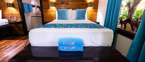 A wooden-paneled room with a bed, two bedside lamps, a mirror, and a view of trees.