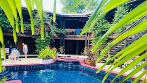 A swimming pool with a tiled edge, surrounded by lush greenery and a wooden building with a balcony. - Mango Inn Resort  (Isla de Utila)