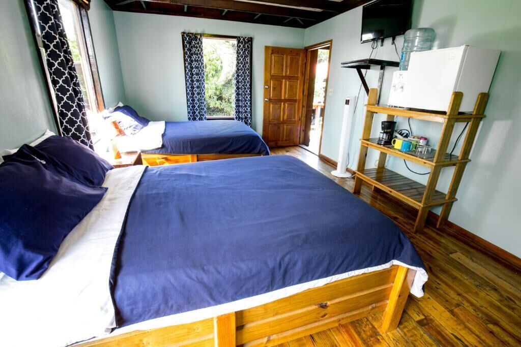 Una habitación con dos camas de madera, un estante de madera con objetos, una puerta y un televisor en la pared.
