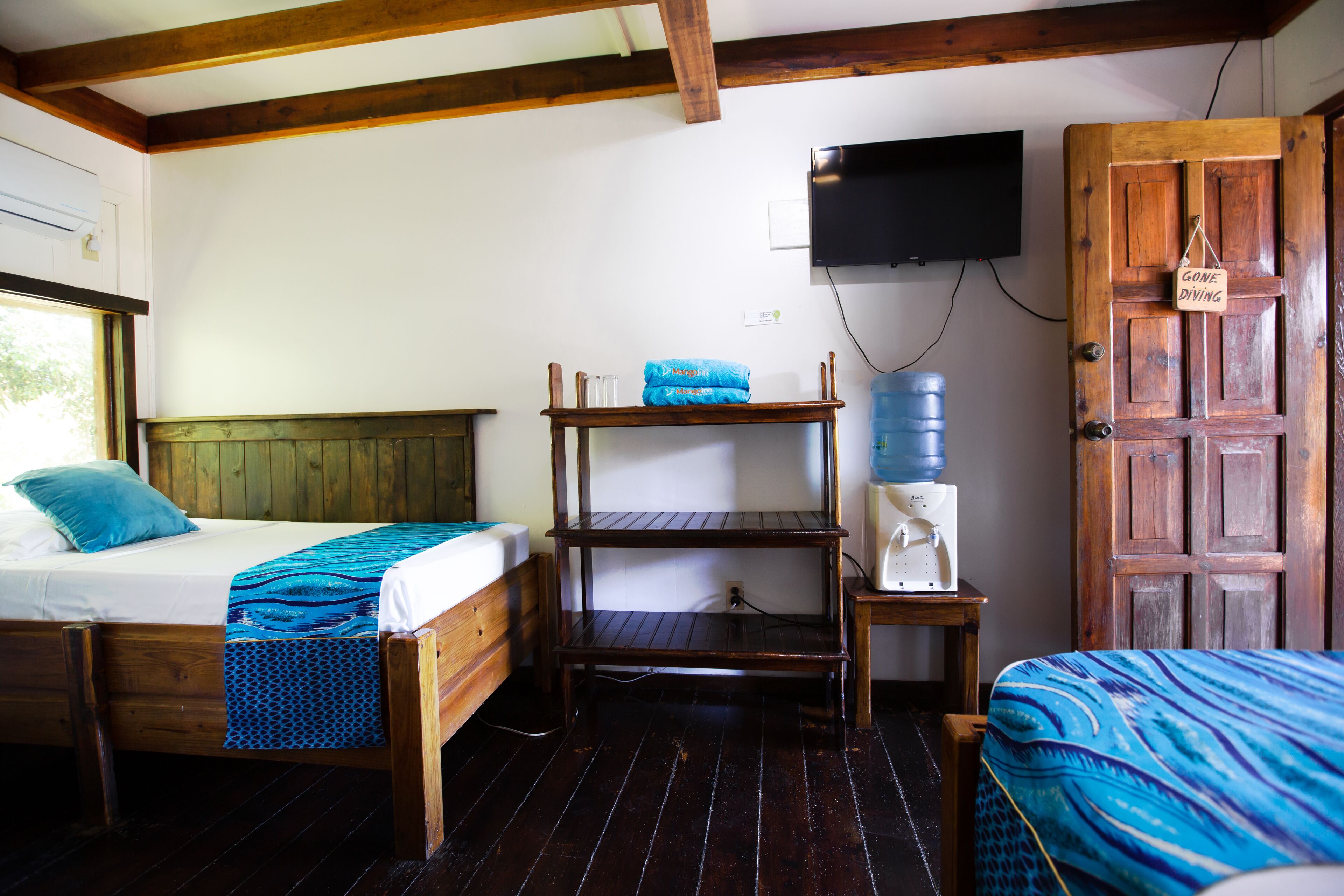 A room with two wooden beds, a wooden shelf with a water dispenser, and a television mounted on the wall.