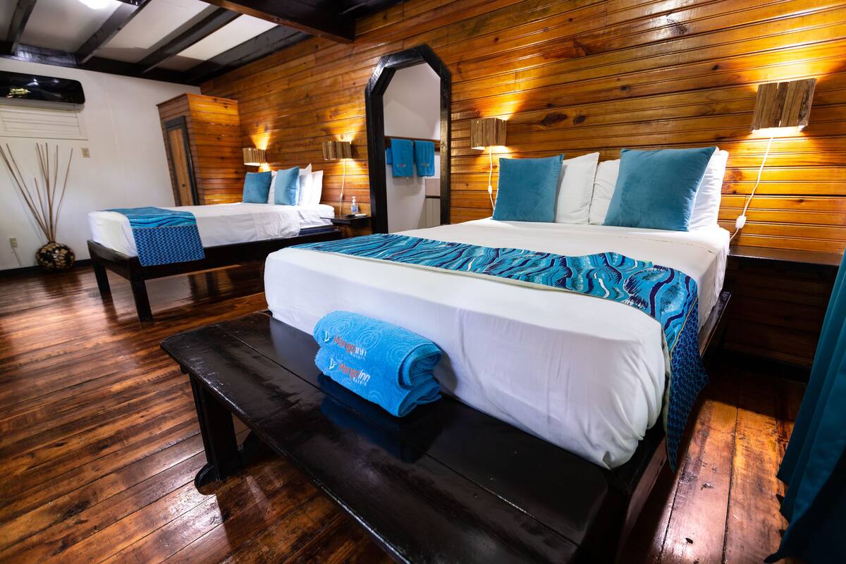 A wooden-paneled room with two beds, a bench, and a mirror.