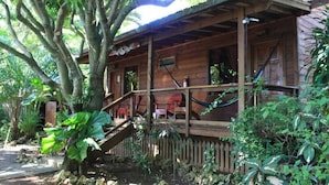 A wooden cabin with a porch, surrounded by lush greenery and a stone pathway. - Mango Inn Resort  (Isla de Utila)
