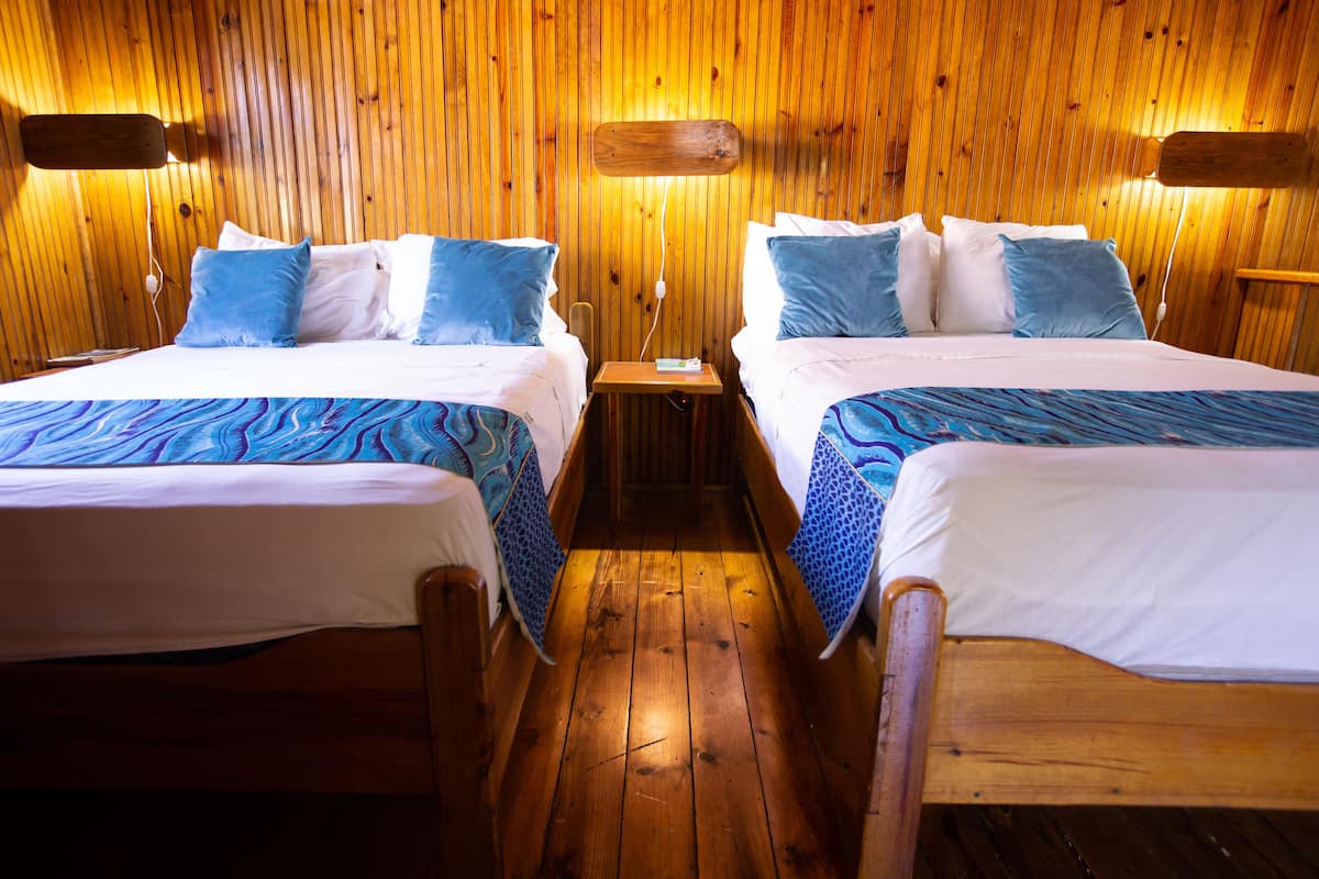 A wooden-paneled room with two beds, each with blue and white bedding.