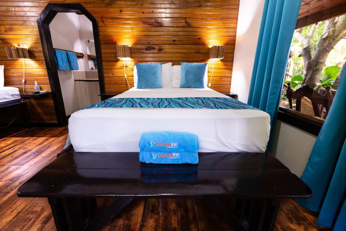 A wooden-paneled room with a bed, a mirror, and a window with curtains.