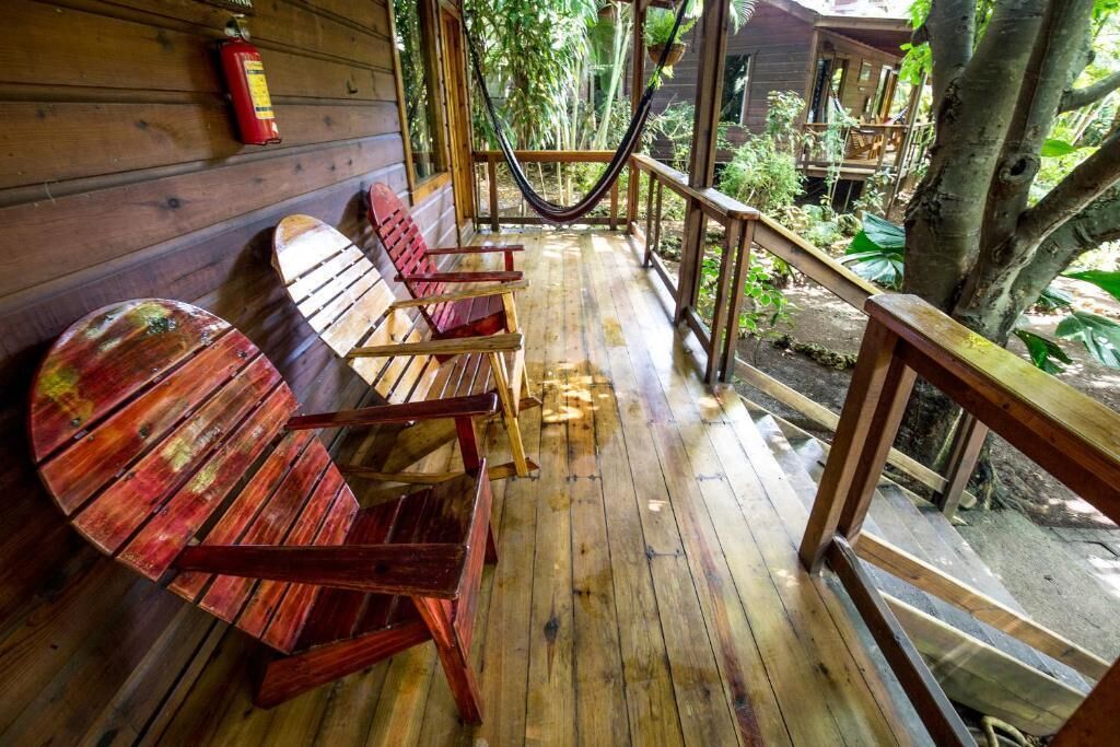 Una terraza de madera con una hamaca, sillas de madera y un extintor.