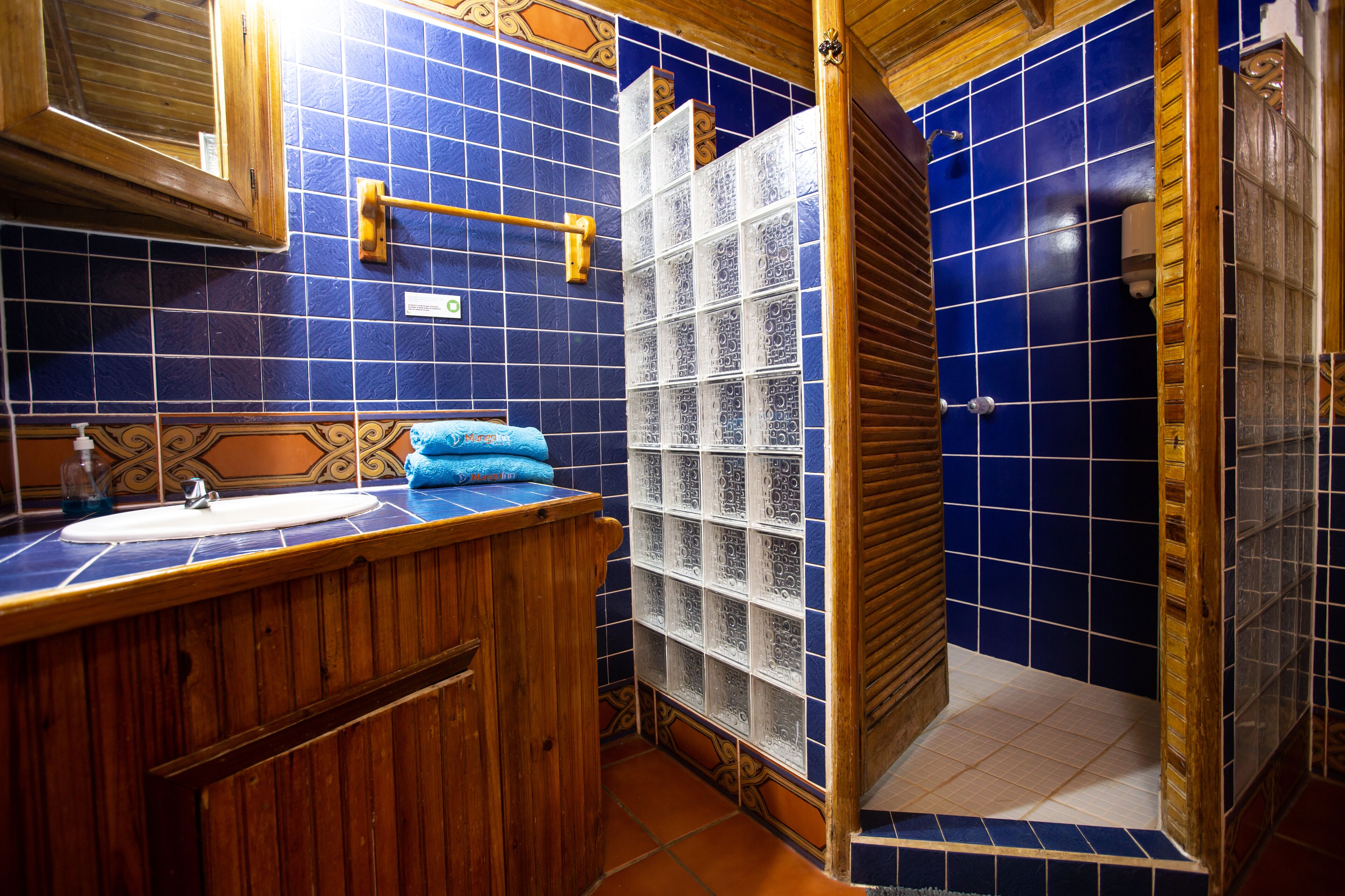 Un baño con tocador de madera, lavamanos y zona de ducha con azulejos azules.