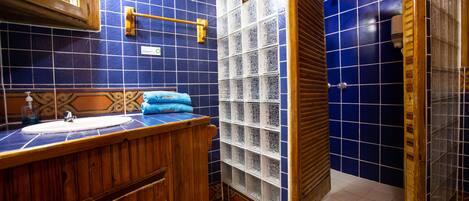Un baño con tocador de madera, lavamanos y zona de ducha con azulejos azules.