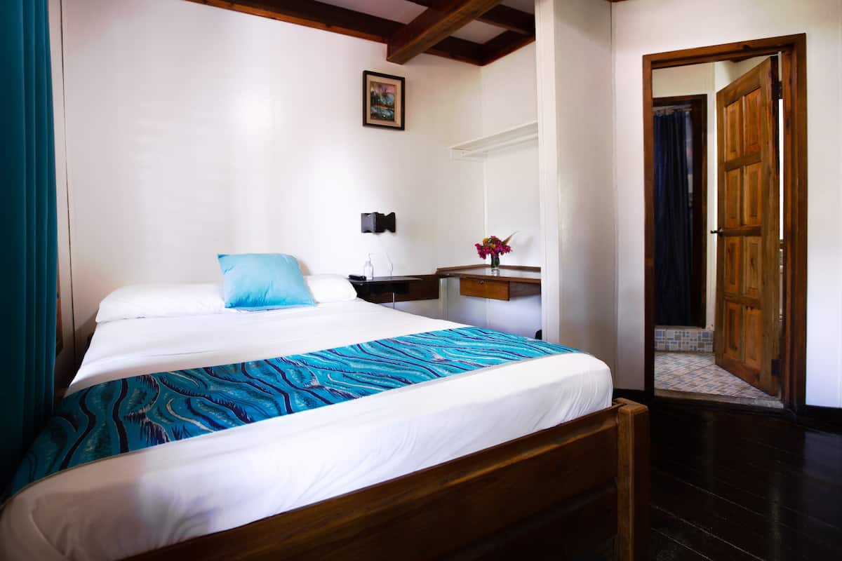 A hotel room with a bed, a nightstand, a mirror, and a door leading to another room.