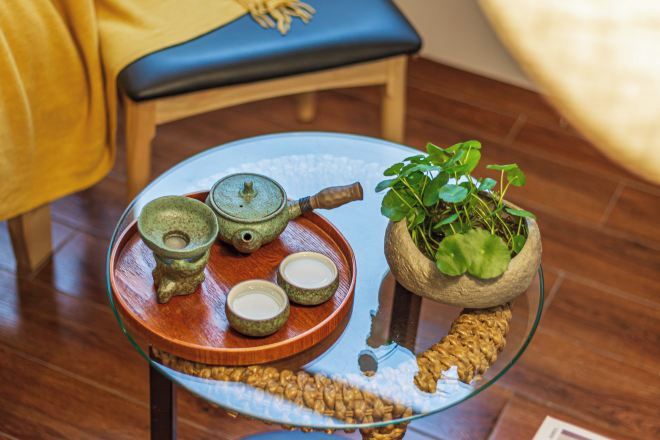 A glass table with a tray holding a teapot, cups, and a plant in a pot.