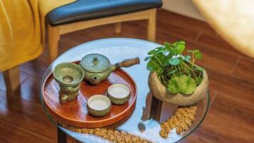 A glass table with a tray holding a teapot, cups, and a plant in a pot.