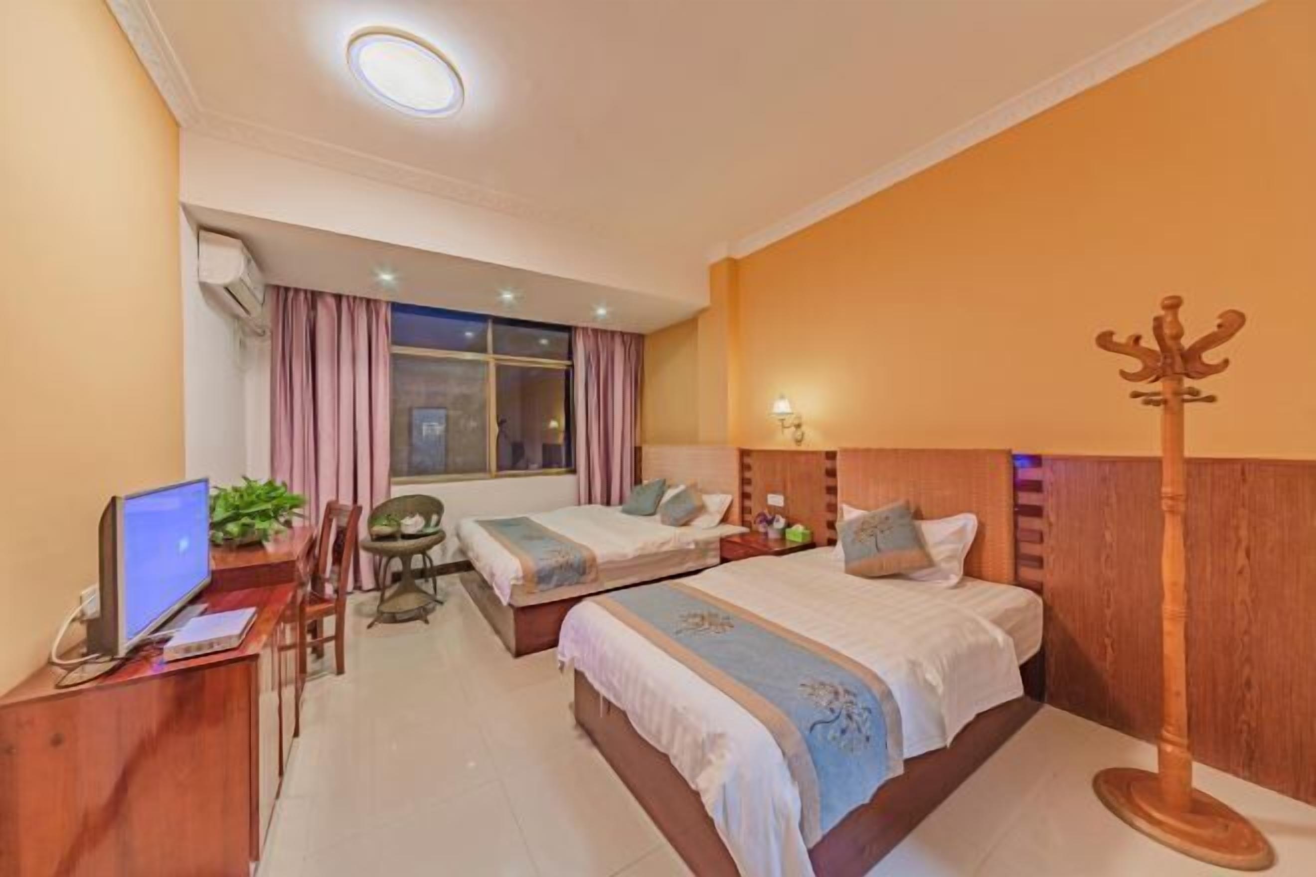 Une chambre d’hôtel avec deux lits, un bureau avec un ordinateur, une chaise, un porte-manteau et une fenêtre avec des rideaux.