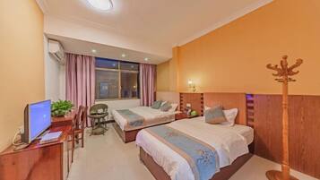Une chambre d’hôtel avec deux lits, un bureau avec un ordinateur, une chaise, un porte-manteau et une fenêtre avec des rideaux.