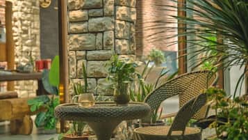 A wicker chair and table set in a room with stone walls and potted plants.
