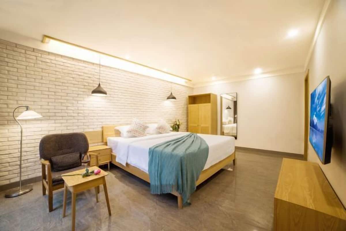 Ein modernes Hotelzimmer mit Backsteinwand, einem Bett mit blauer Decke, einem Schreibtisch mit Lampe und einem an der Wand befestigten Fernseher.
