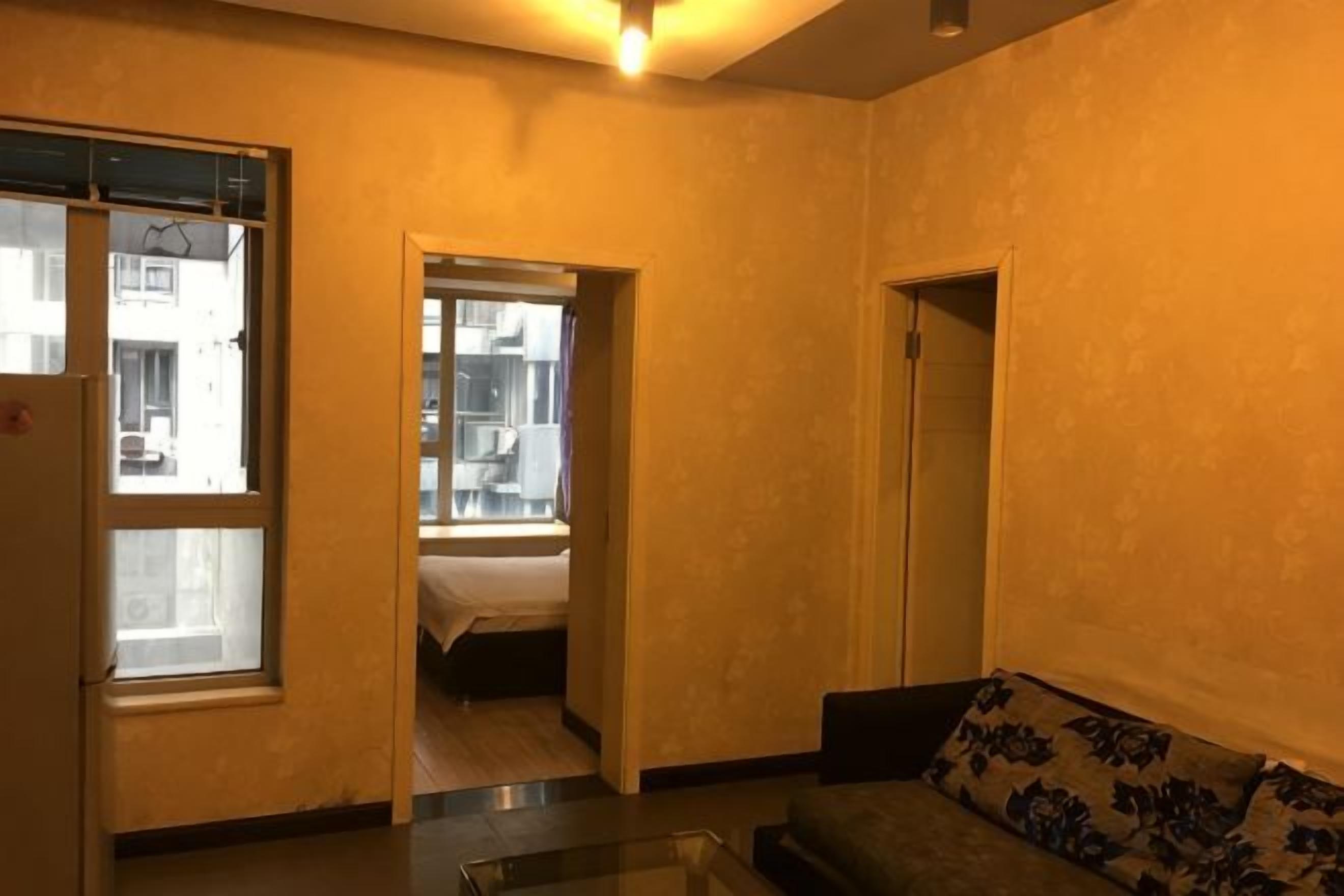 A living room with a sofa and a glass coffee table. There is a doorway leading to a bedroom.