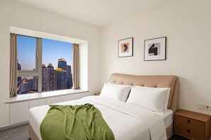 A hotel room with a bed, a window with a city view, a bedside table, and two framed pictures on the wall. - Chongqing Ruika Apartment (Guanyinqiao Pedestrian Street) (Chongqing)