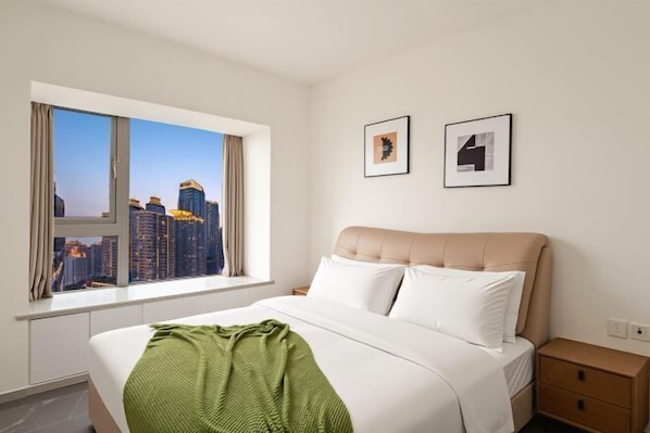 A hotel room with a bed, a window with a city view, a bedside table, and two framed pictures on the wall.