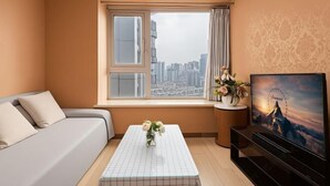 Ein modernes Zimmer mit einer Couch, einem kleinen Tisch mit Blumenvase, einem Fernseher und einem Fenster mit Stadtblick.