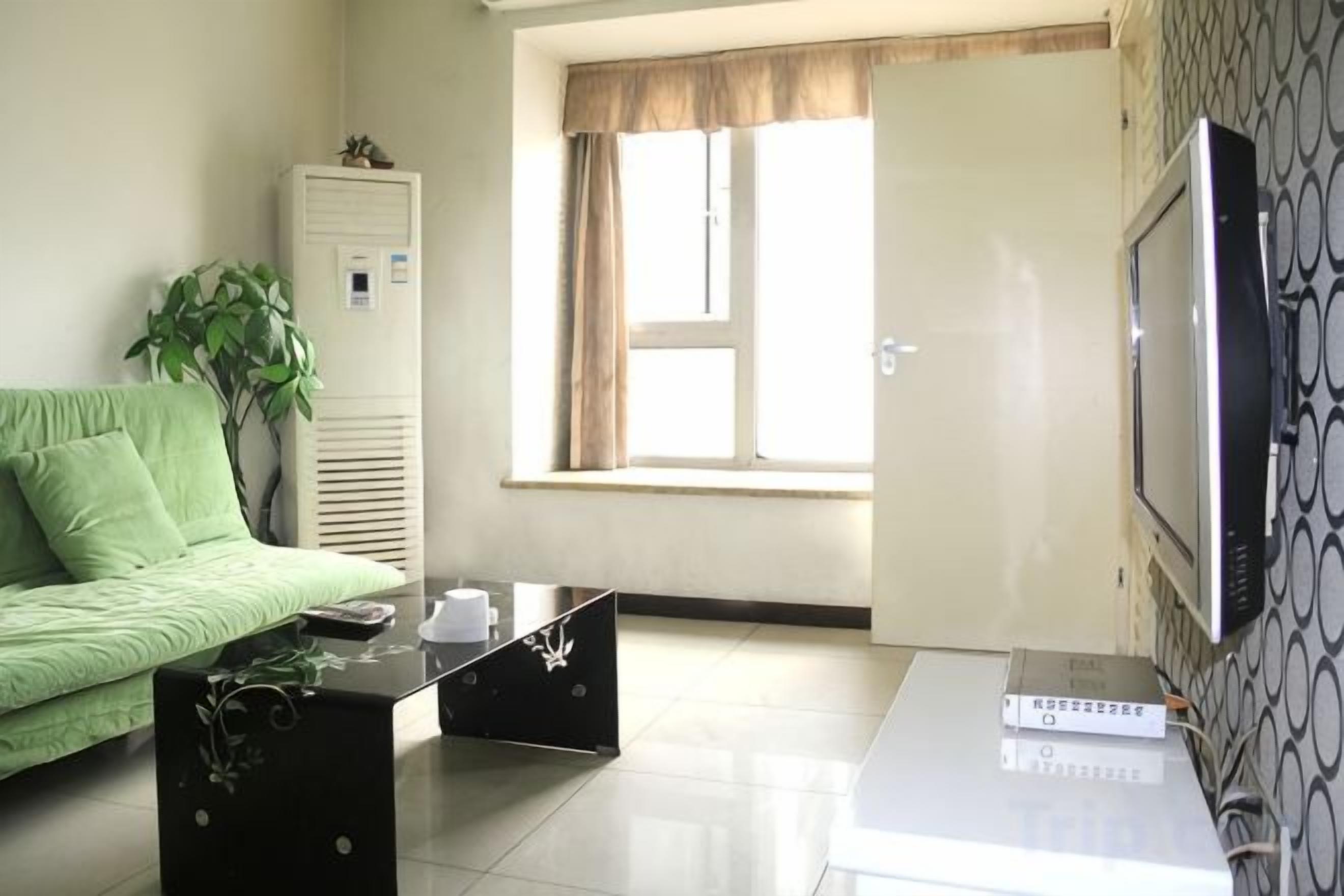 A room with a green sofa, a coffee table, a TV, and a window with curtains.