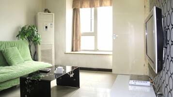 A room with a green sofa, a coffee table, a TV, and a window with curtains.