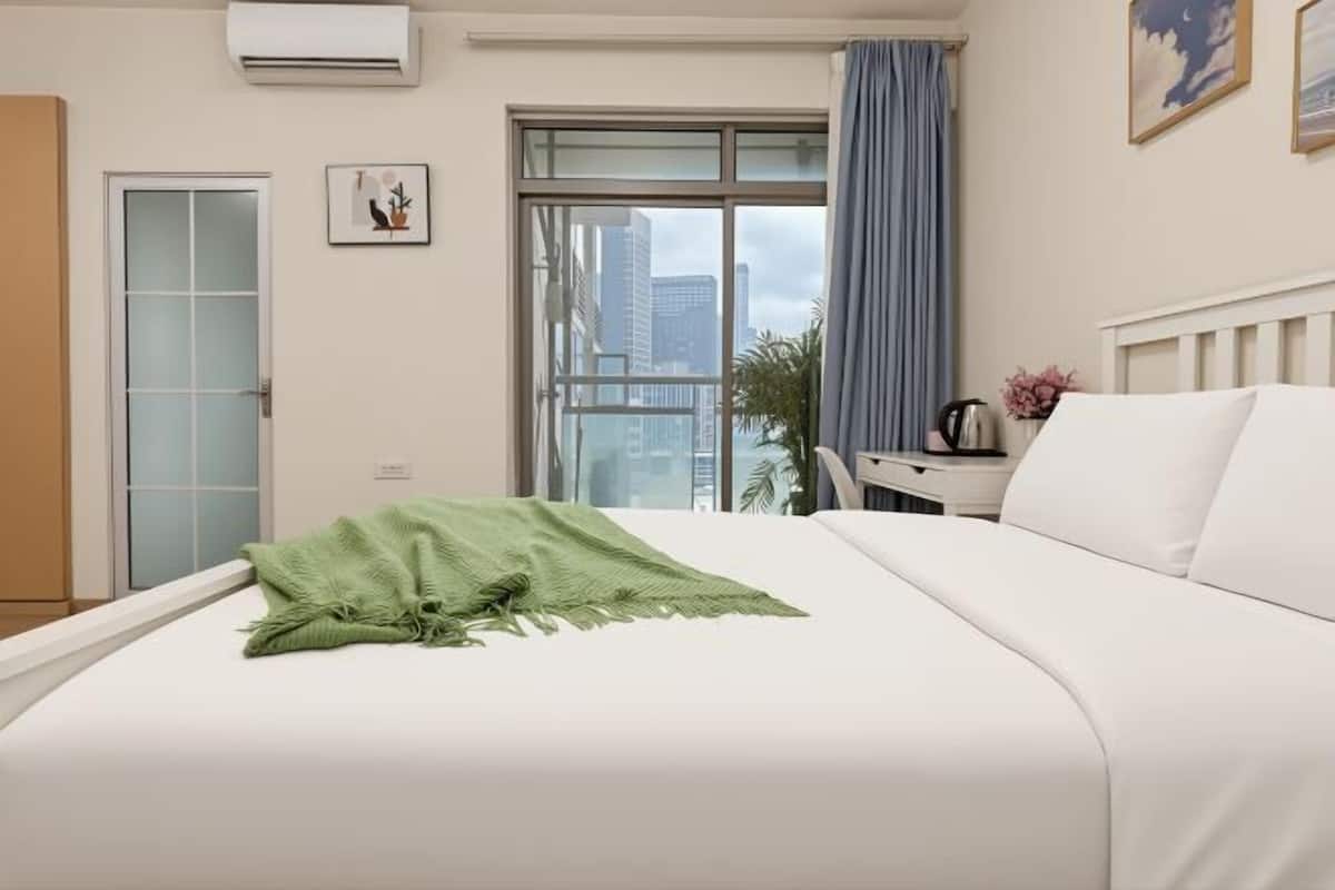 Ein Hotelzimmer mit Bett, Schreibtisch, Fenster und Blick auf Gebäude sowie einer Klimaanlage.