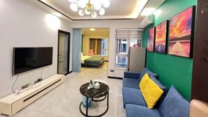 Ein modernes Wohnzimmer mit Flachbildfernseher, Couchtisch, Sofa und einer Deckenleuchte.