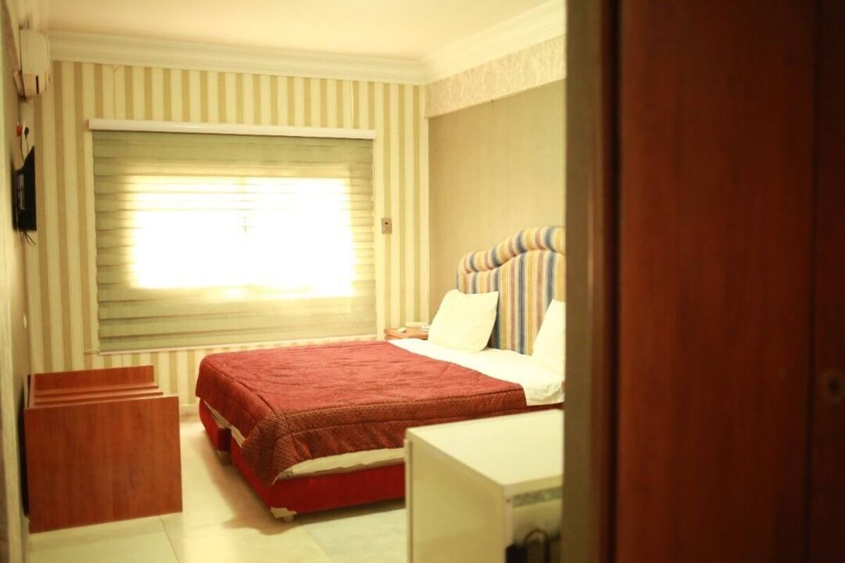 A bedroom with a bed, a bedside table, a window with blinds, and a wooden cabinet.