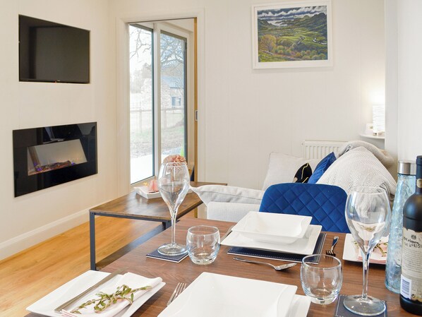 A dining area with a table set for two, a painting on the wall, and a TV mounted on the wall.