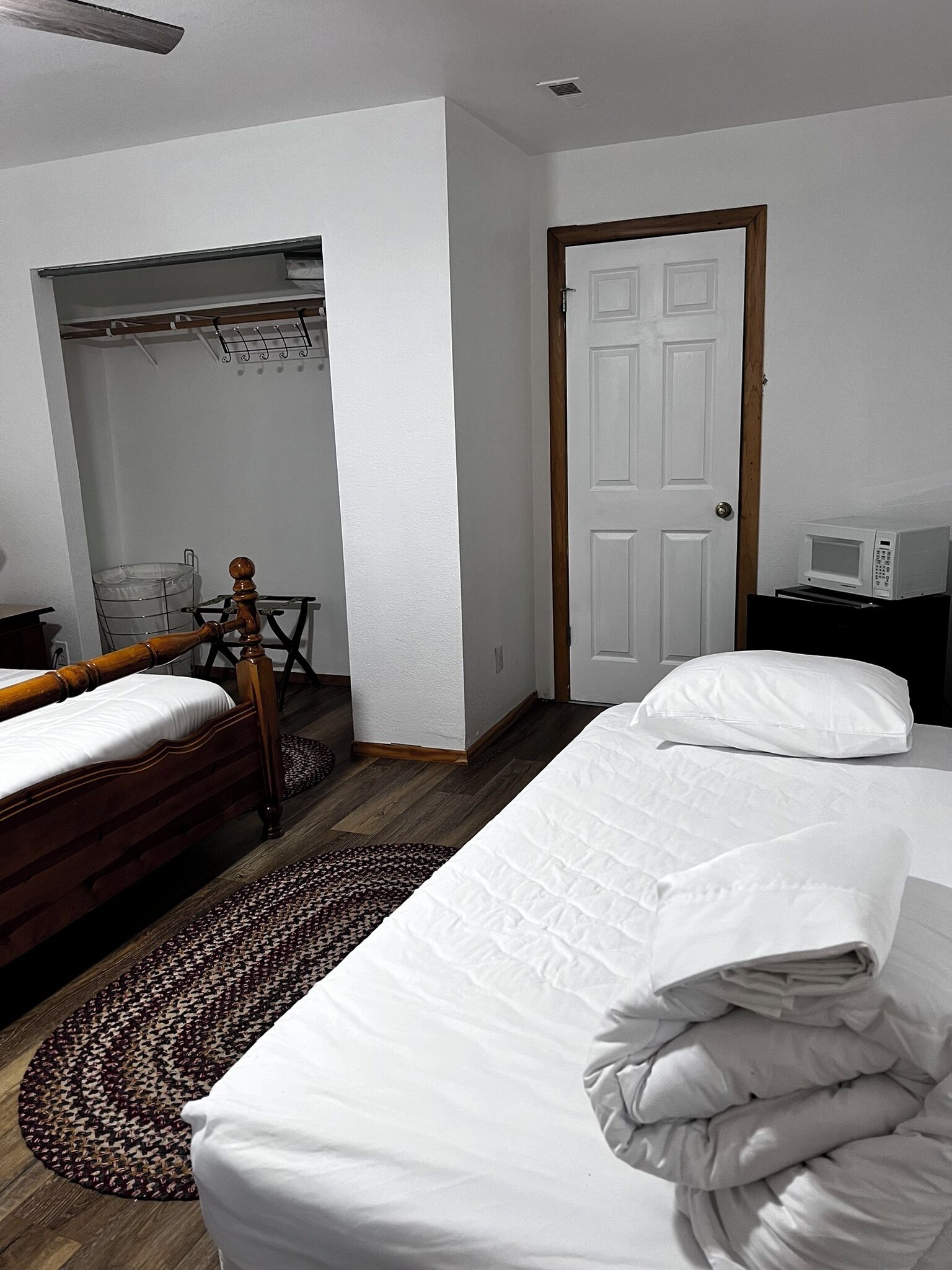 A hotel room with two single beds, a wooden chair, a small table with a microwave, a closet, and a door.
