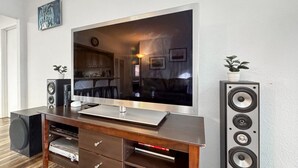 Un salon avec un téléviseur à écran plat posé sur un meuble de rangement en bois, deux enceintes sur pied et une plante en pot.