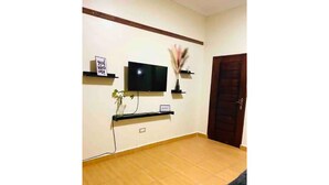 Una sala de estar con un televisor de pantalla plana montado en la pared, una puerta de madera y un piso de baldosas.