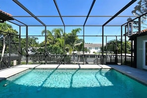 A swimming pool with a glass enclosure, surrounded by a fence and palm trees. - Peaceful, Siesta Keywaterfront home, elegantly decorated, ideal for families. (Siesta Key)