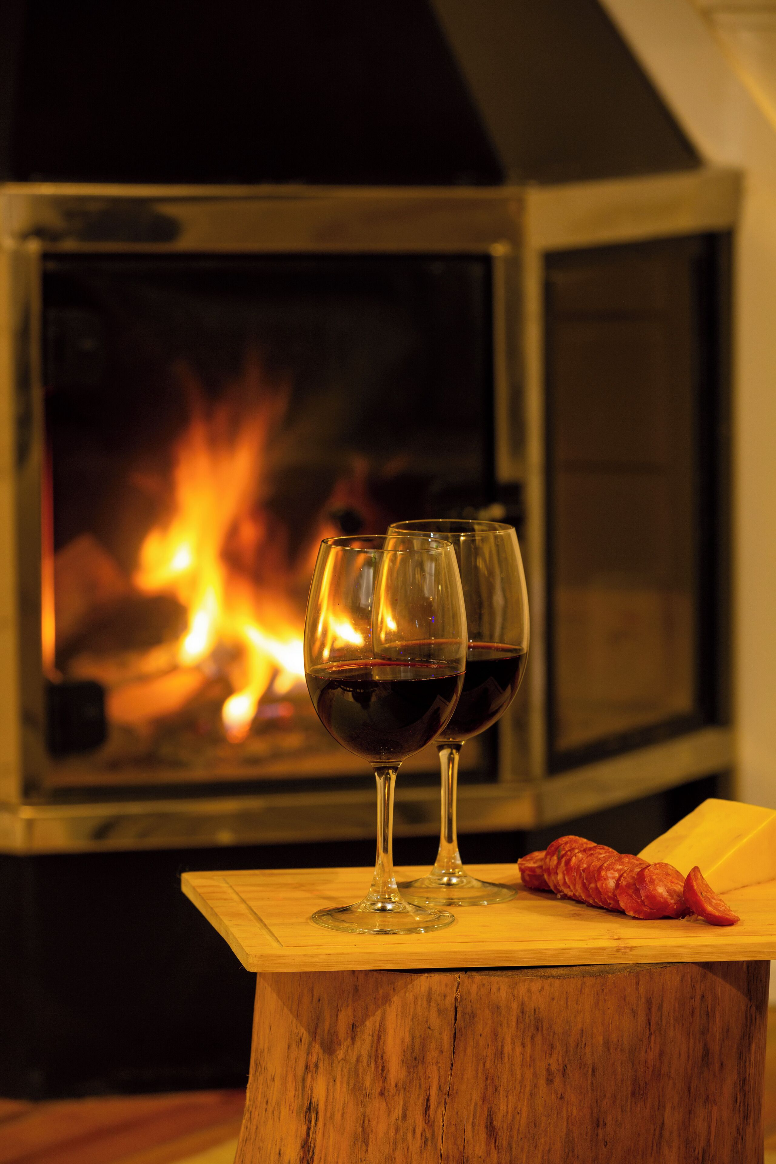 Dos copas de vino sobre una mesa de madera con un fuego de fondo.