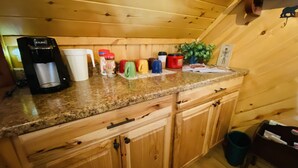 Cocina con armarios de madera, encimera de granito, cafetera Keurig y varias tazas y recipientes.
