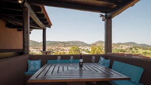 A wooden table with a wine bottle and glasses on a terrace with a view of a town and hills. - Il Vecchio Faro Attico A5 (Loiri Porto San Paolo)