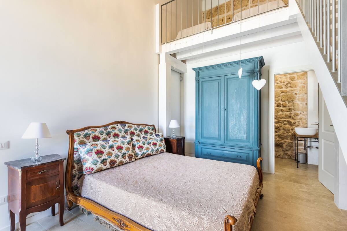 A bedroom with a bed, a nightstand, a dresser, and a staircase.