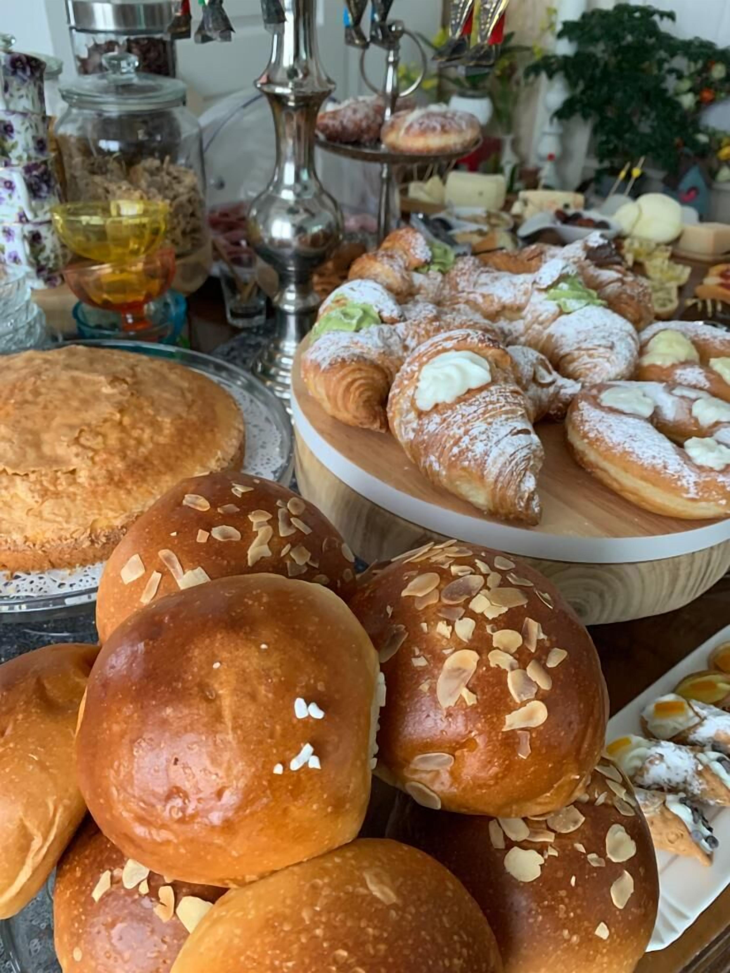 Variedad de productos horneados, incluyendo bollos de pan, croissants y pastelería, sobre una mesa de madera.