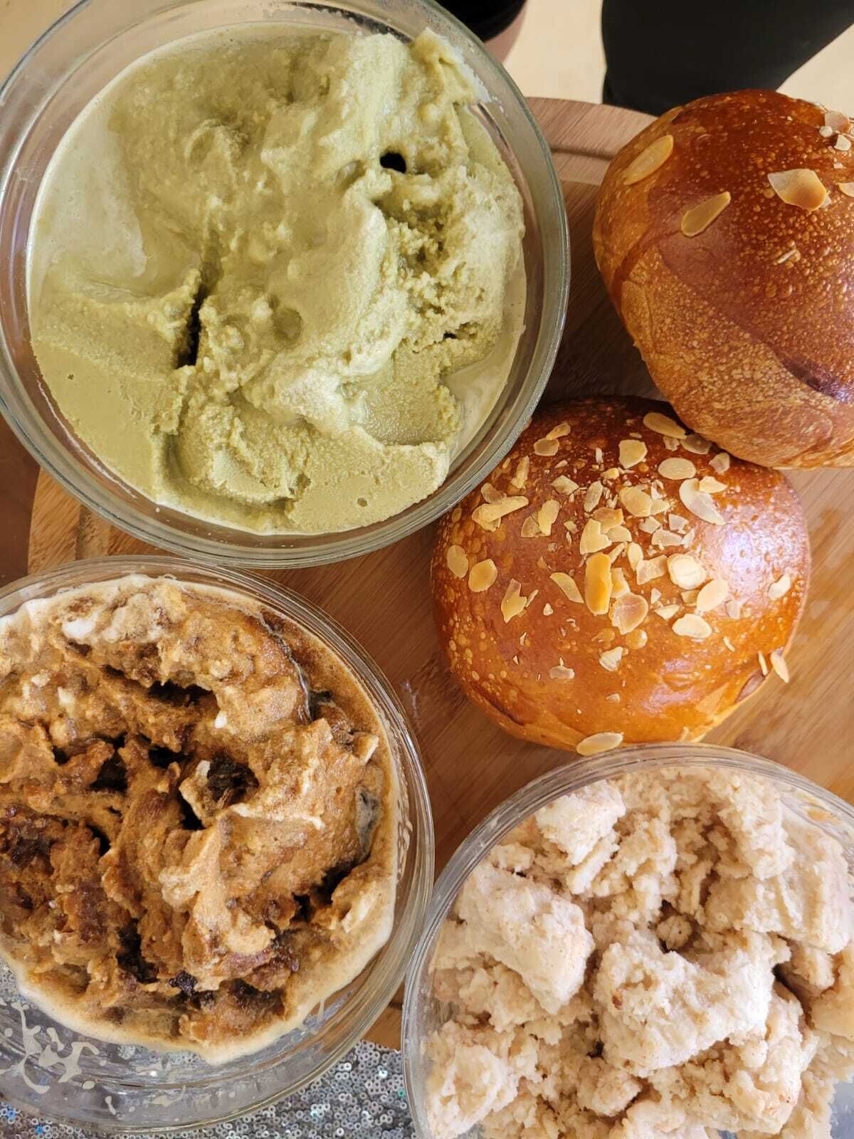 Una mesa de madera con cuatro cuencos de diferentes alimentos, incluyendo un postre verde, un postre marrón con pasas y un postre blanco.