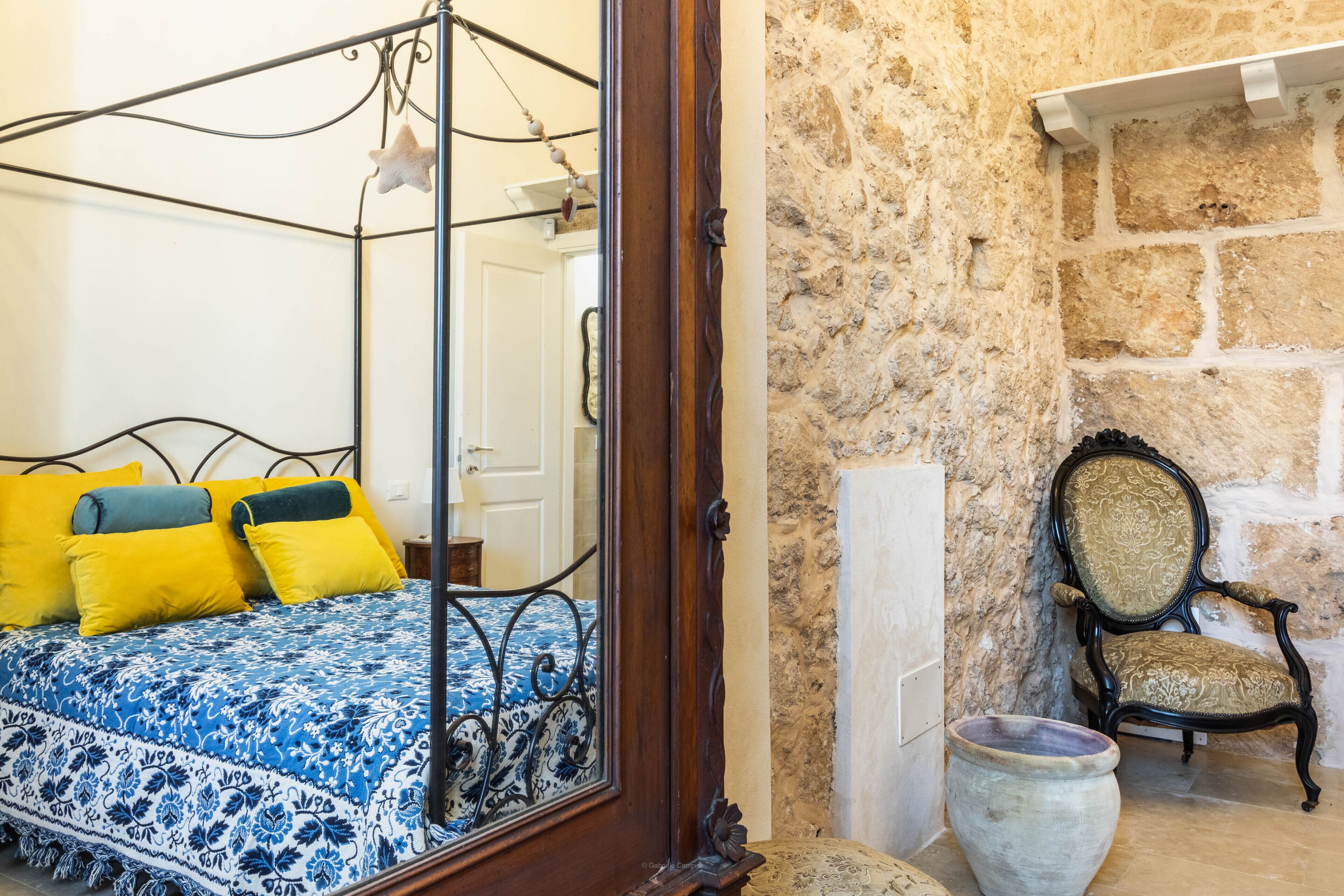 Une chambre à coucher avec un lit à baldaquin, un mur en pierre, une chaise et un grand vase.