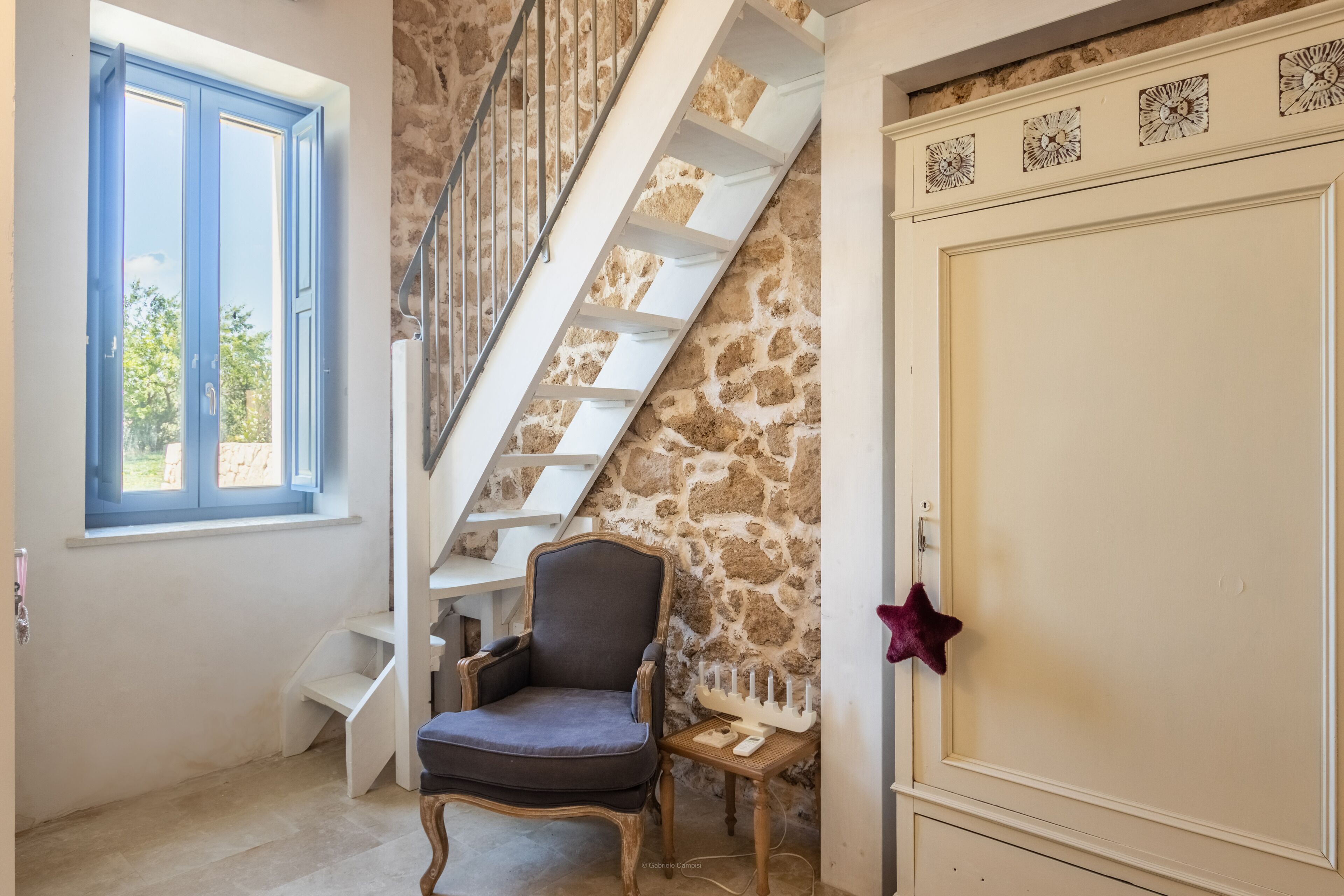 A room with a stone wall, a wooden chair, a white staircase, and a door with a star decoration.
