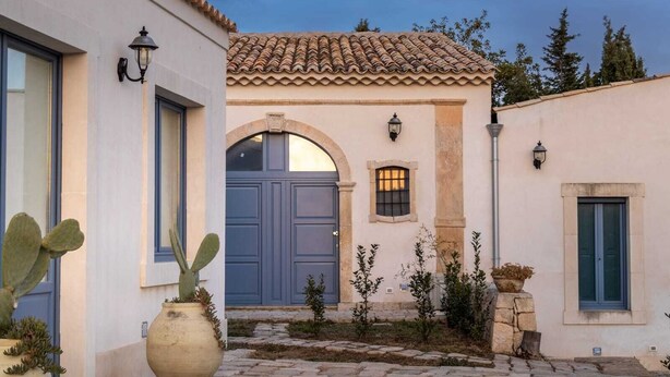 A building with a tiled roof, a central archway, and a cobblestone courtyard. - Michael Garden (Noto)