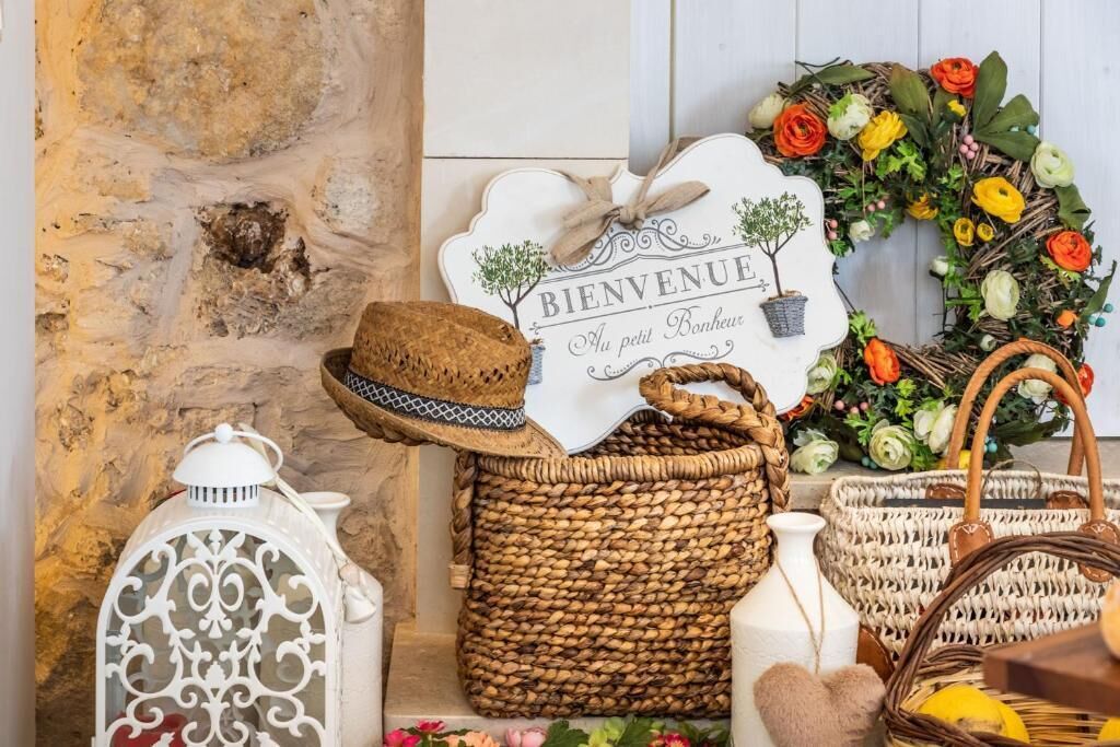 Un interior rústico con pared de piedra, cestas de mimbre, un farol, un cartel de bienvenida y una guirnalda floral.