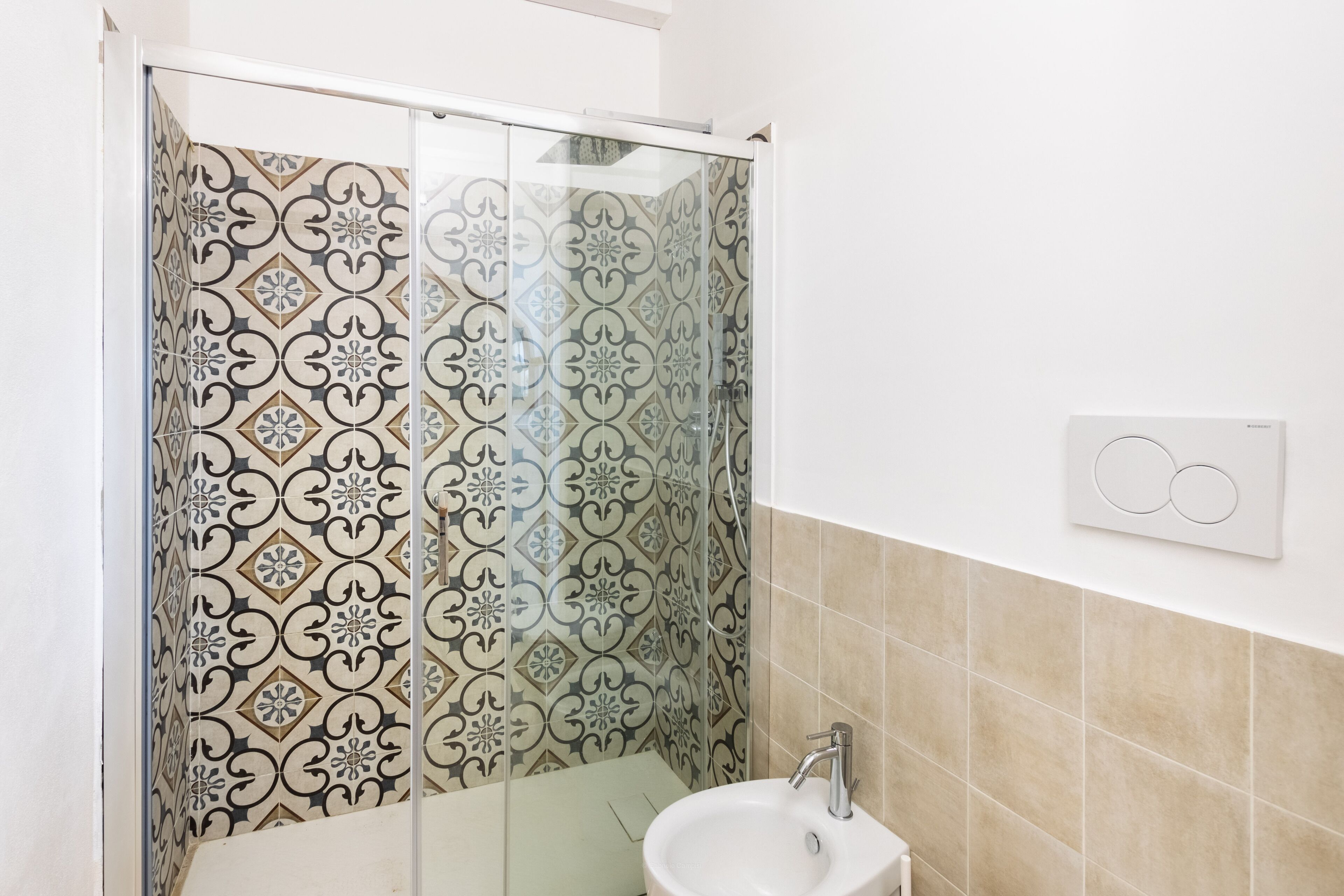 A bathroom with patterned tiles, a glass shower enclosure, and a sink with a wall-mounted light switch.