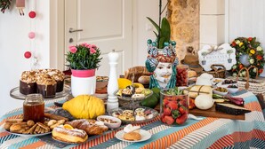 A table with various food items and decorations, including pastries, fruits, and a vase with flowers. - Michael Garden (Noto)