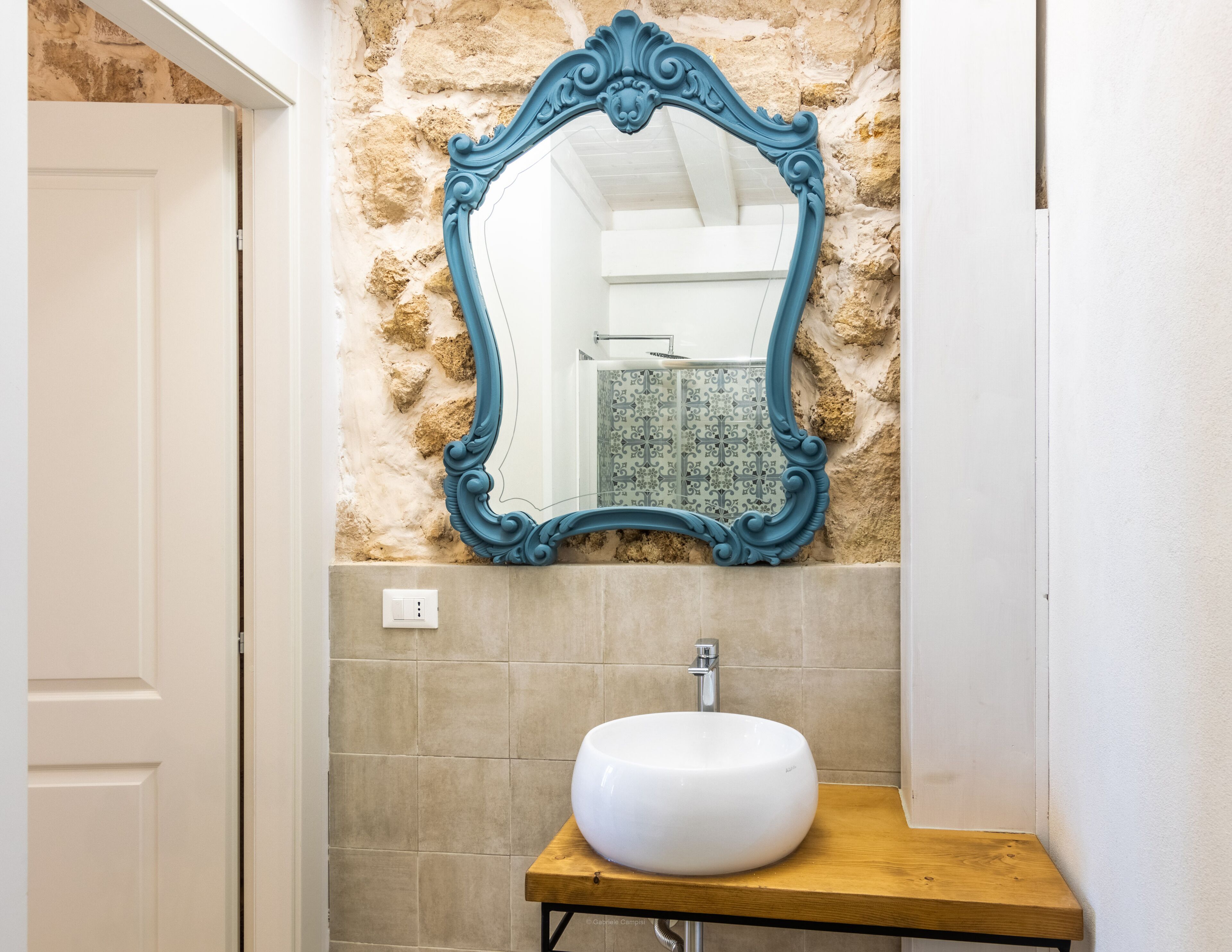 A bathroom with a white sink, a blue ornate mirror, and a stone wall.