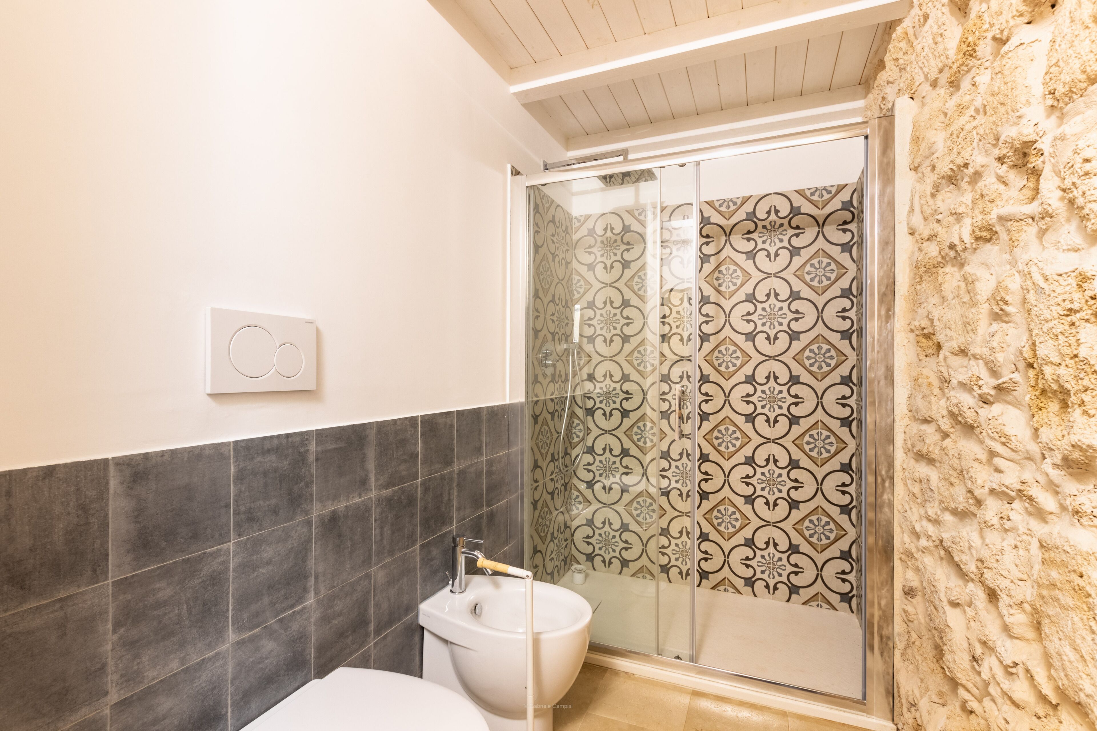 Baño con inodoro, bidé y zona de ducha con baldosas estampadas.