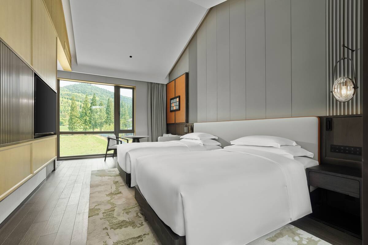 Una habitación de hotel moderna con una cama grande, un escritorio y vistas a un paisaje verde.