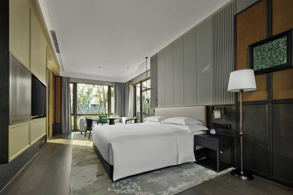 Una habitación de hotel moderna con una cama grande, mesitas de noche, una lámpara y vistas al exterior.