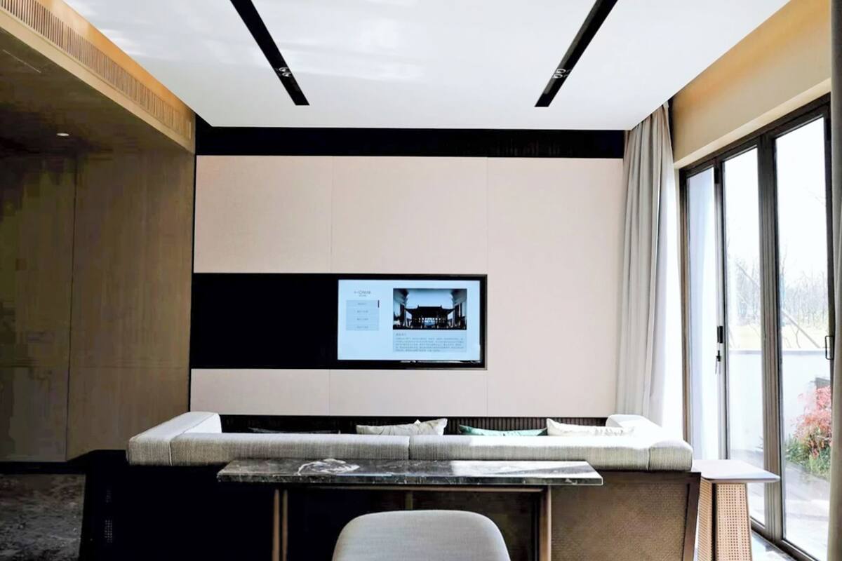 Habitación de hotel moderna con un ventanal grande, un banco empotrado y un televisor de pantalla plana en la pared.