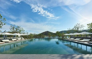Une piscine aux eaux cristallines, bordée de chaises longues et d’ombrelles, et entourée d’arbres et de collines.